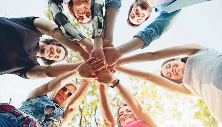 Low angle view of a group joining hands in a circle, shot against a bright sky.