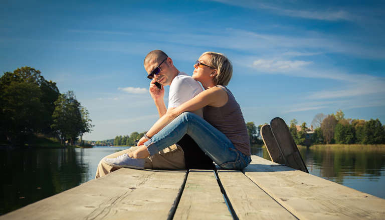 Couple on pier; man on the phone, woman leaning on him.