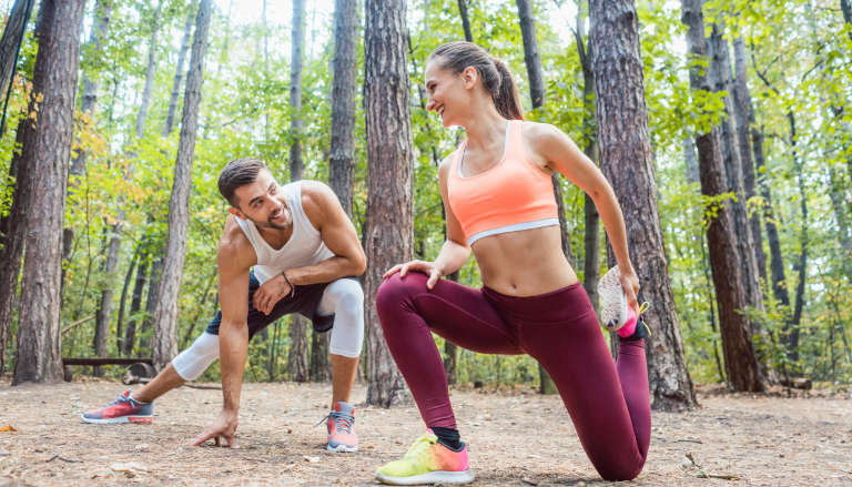 A man and woman stretching in a forest.