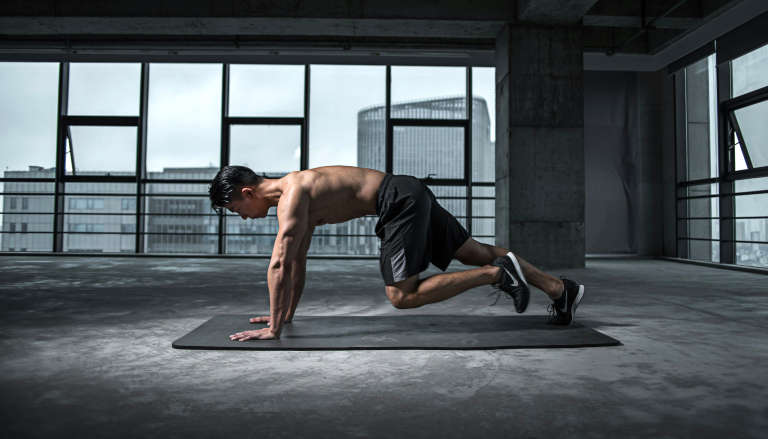 Athletic man in quadrupedal position performing bodyweight exercise.
