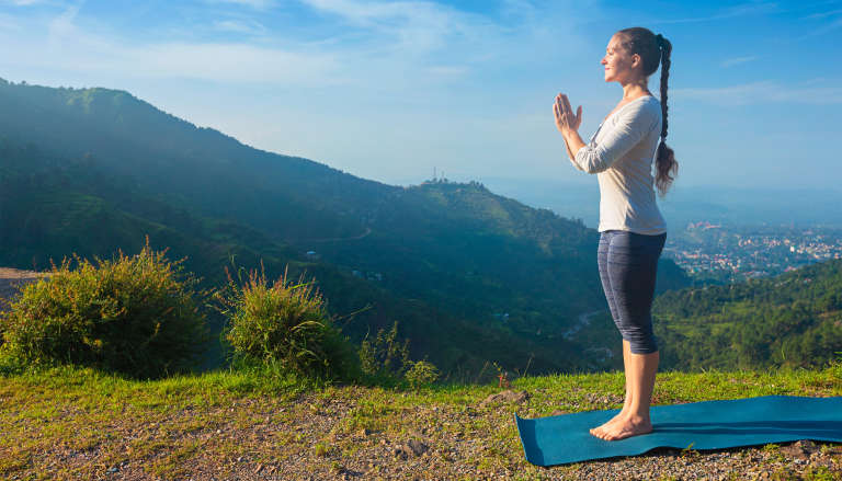 Woman practicing yoga mountain pose on a hilltop.