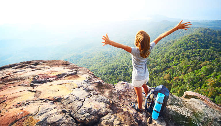 Woman on a mountain top with arms out stretched.