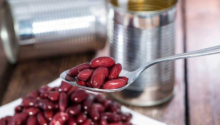 Tinned kidney beans on a spoon with cans.