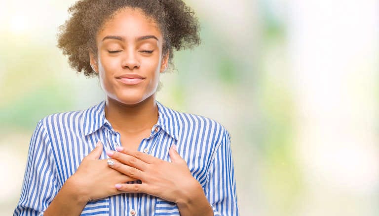 Young woman with her hands on heart and a smile on her face.