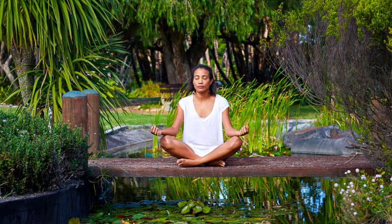 Woman meditating by a serene pond in nature.