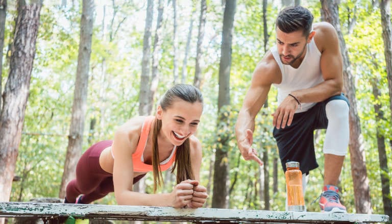 Woman doing a plank exercise outside in nature with her partner.